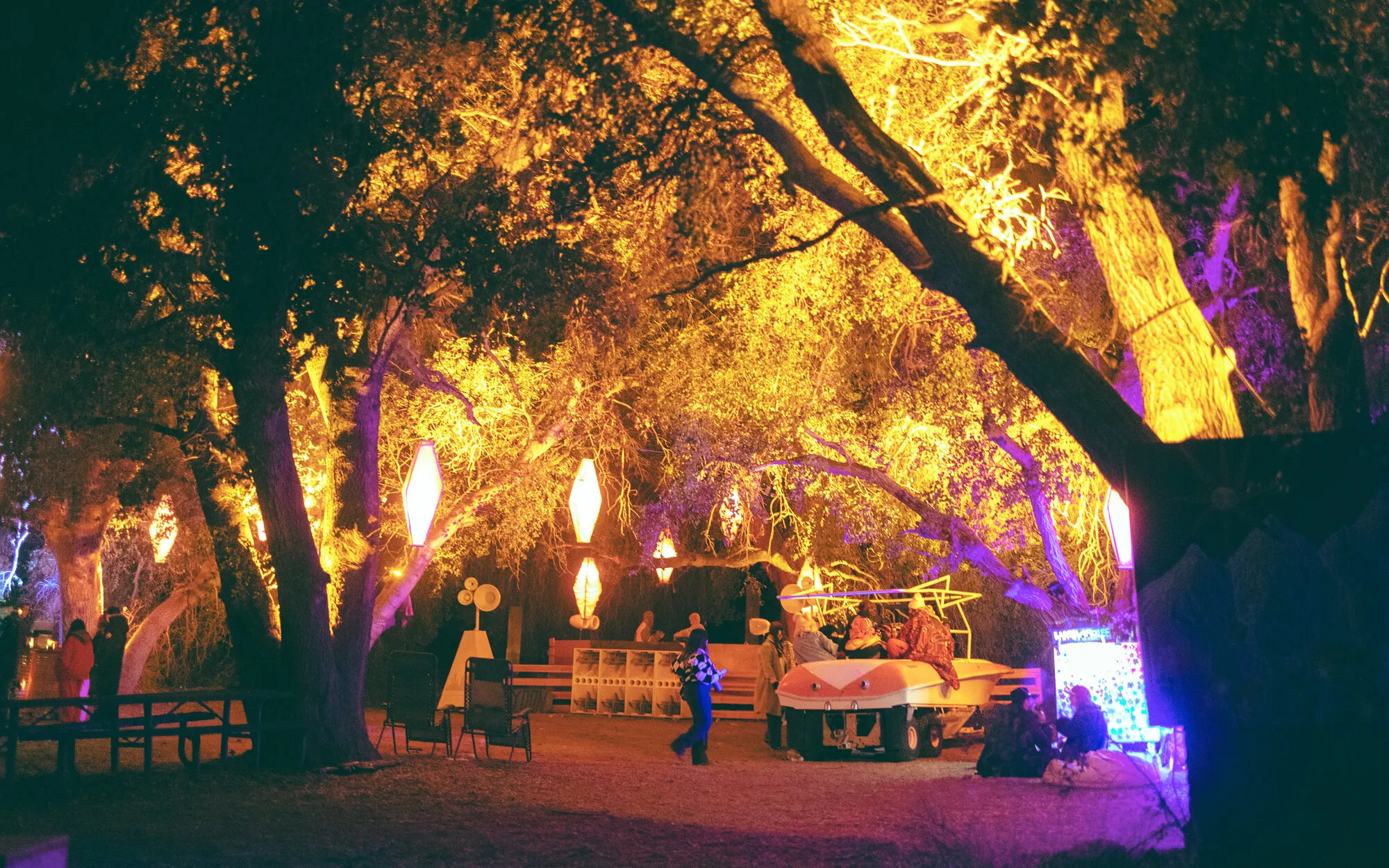 The Woods stage lit orange and purple under oak trees at night